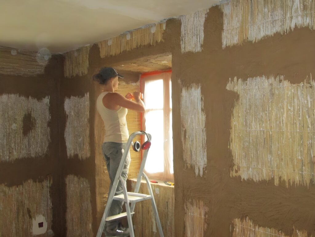 Étape de finition avant l'application d’un enduit terre sur une paroi intérieure en panneaux de roseau autour d’une fenêtre